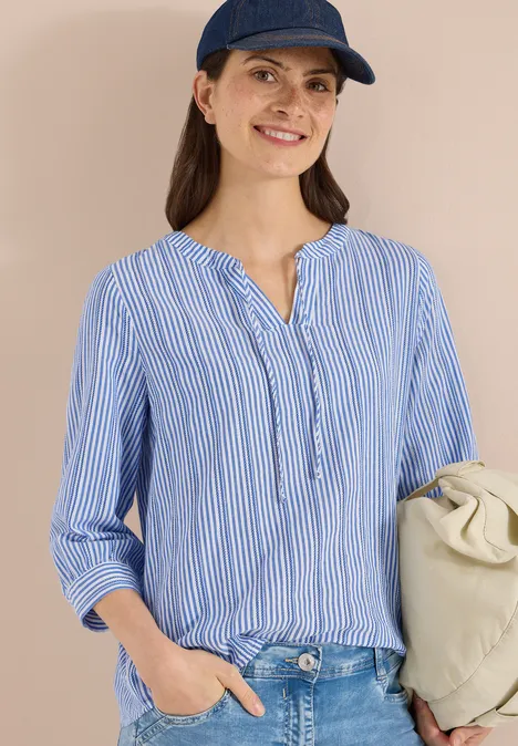 Person trägt blau-weiß gestreifte Bluse, Jeans, blaue Kappe und helle Schultertasche.