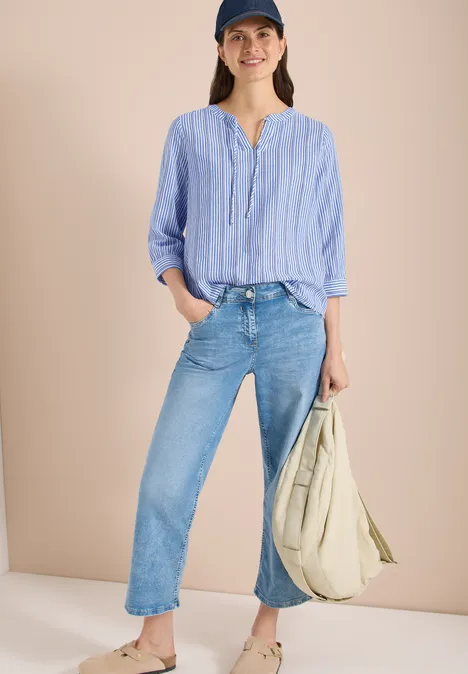 Frau in hellblau-weiß gestreiftem Hemd, leger in gerade Jeans gesteckt, mit großer beigefarbener Stofftasche.