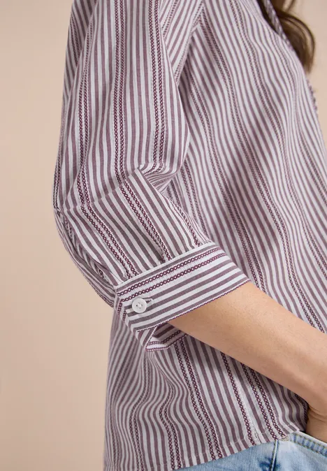Nahaufnahme eines gestreiften Hemdes mit hochgekrempeltem Ärmel, kombiniert mit Jeans.