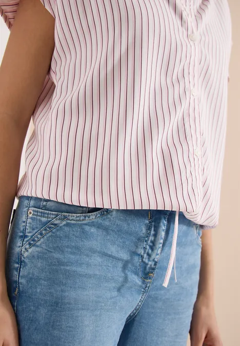 Eine Person trägt eine rosa-weiß gestreifte Bluse und blaue Jeans.