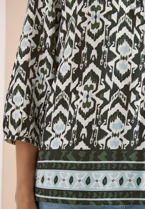 Nahaufnahme eines grünen, schwarz-weißen Ethno-Musters auf einem langärmligen Kleidungsstück.