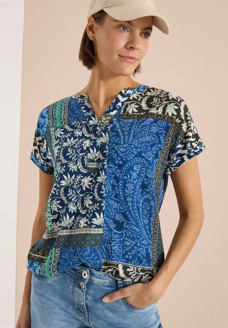 Eine leichte Patchwork-Bluse mit blau-weißem Paisley- und Blumenmuster, kurzen Ärmeln und V-Ausschnitt.