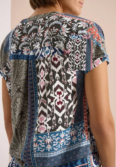 Vrouw van achteren in een kleurrijke patchworktop met bloem- en geometrische patronen.