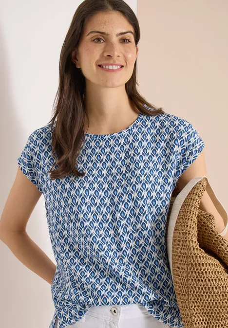 Frau trägt blau-weiß gemustertes T-Shirt und hält einen geflochtenen Korb in der Armbeuge.