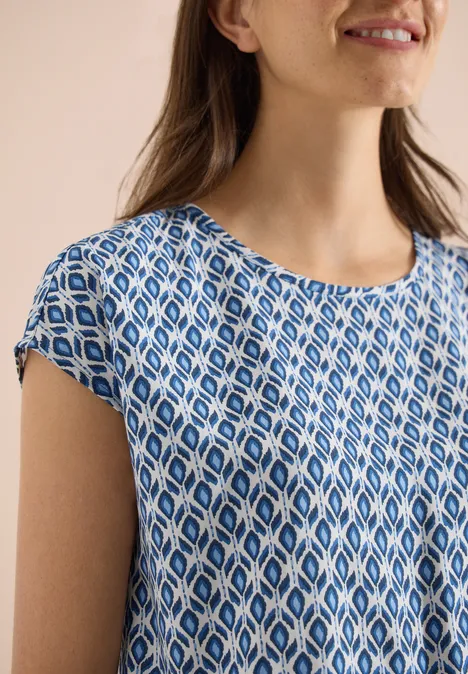 Nahaufnahme einer Frau in blau-weiß gemustertem, kurzärmeligem Oberteil.