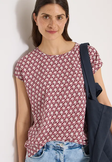 Een vrouw draagt een rood-wit dessin top met korte mouwen en een donkerblauwe schoudertas.