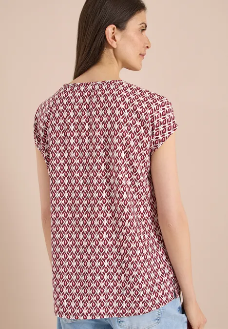 Vrouw van achteren in rood-wit geometrisch dessin T-shirt met korte mouwen voor beige achtergrond.