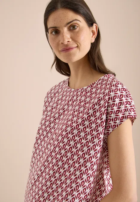 Vrouw draagt los T-shirt met rood-wit ruitpatroon tegen lichte achtergrond