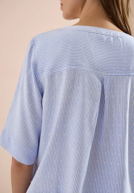 Achteraanzicht van een vrouw in een lichtblauw, fijn gestreept T-shirt met korte mouwen