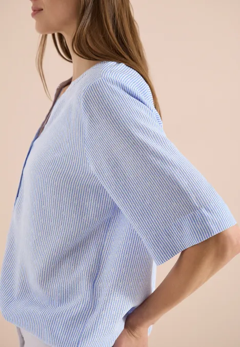 Zijaanzicht van een vrouw in lichtblauwe gestreepte blouse tegen een beige achtergrond.