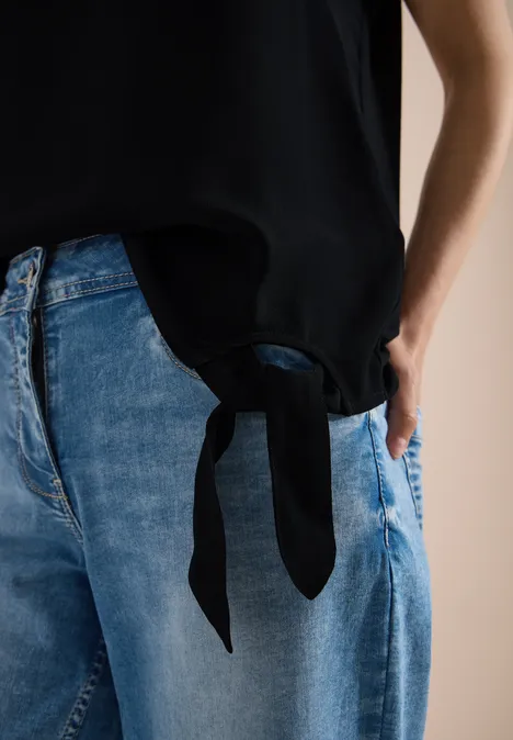 Eine blaue Jeans und ein schwarzes Top mit seitlicher Schleppe an der Taille.