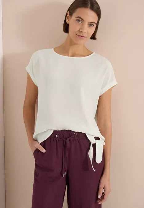 Blouse met ronde hals en knoopdetail vanilla white Persoon draagt wit kort mouwtopje met knoop aan de zijkant en bordeauxrode broek.
