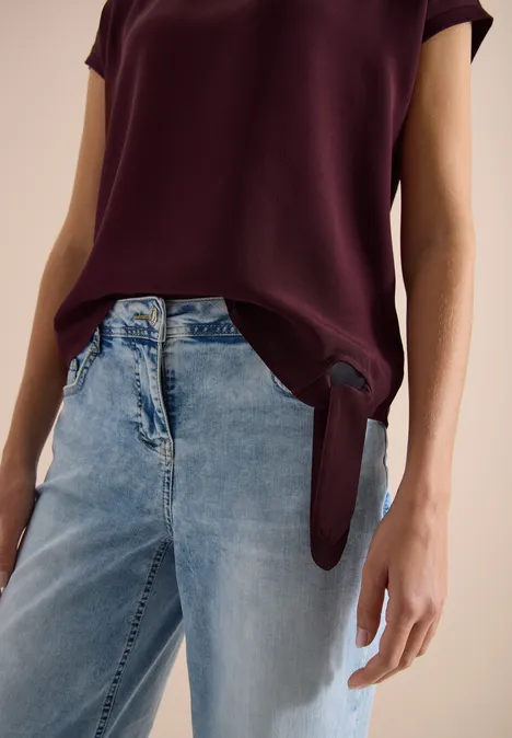 Bluse mit Rundhals und Knotendetail sweet grape red Frau trägt weinrote Bluse, vorne locker gesteckt, zusammen mit weiten hellblauen Jeans.