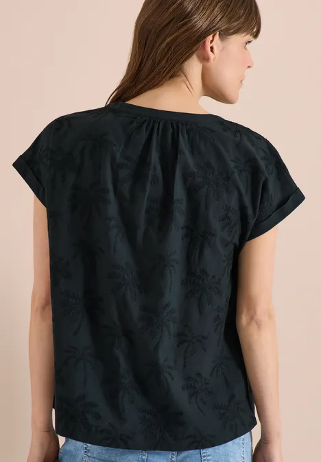 Frau von hinten in lockerem, schwarz besticktem Kurzarmtop mit dezentem Blattmuster.