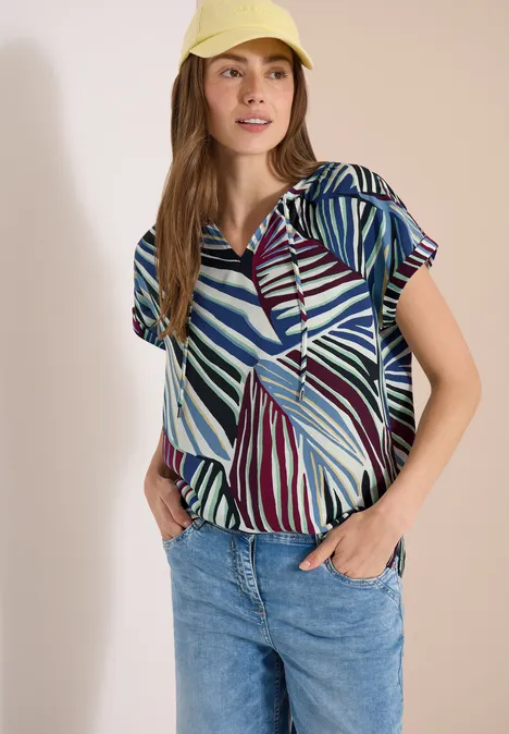 Vrouw in een gemêleerd blouseje en jeans voor een lichte achtergrond.