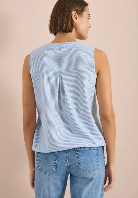 Femme vue de dos portant un top sans manches bleu clair et un jean sur fond neutre.
