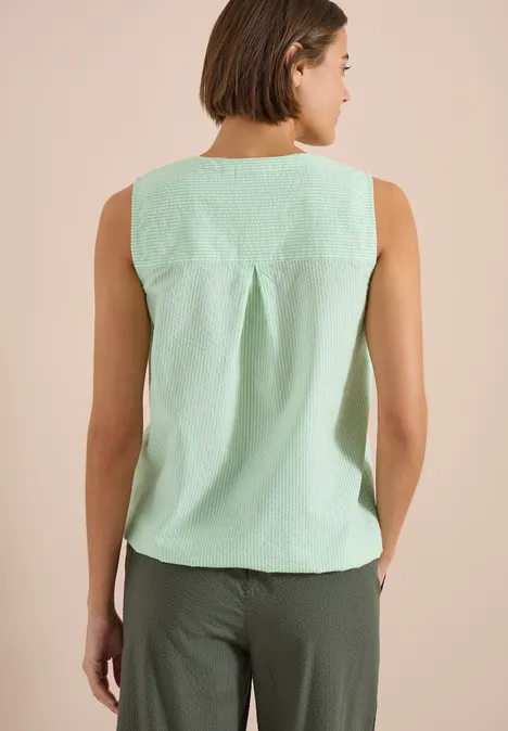Vue de dos d’une femme portant un haut vert menthe et un pantalon foncé sur fond beige.