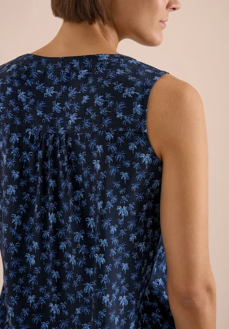 Femme de dos portant un haut sans manches bleu foncé à fleurs bleues et un pli dans le dos.