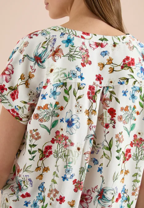 Nahe Ansicht einer weißen Bluse mit buntem Blumenprint und lockerem, gerafftem Rückendetail.