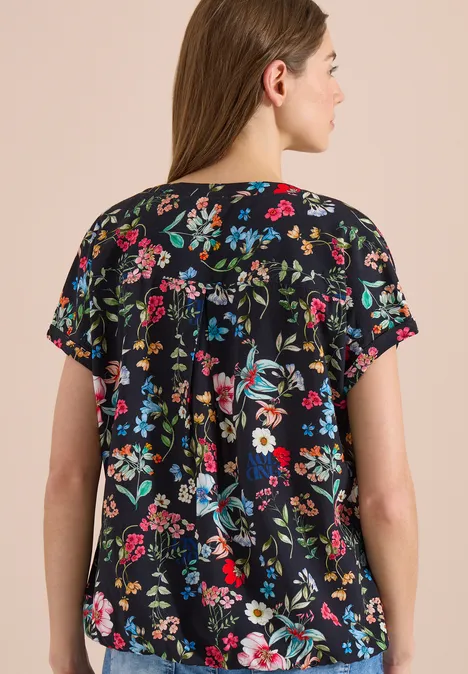 Rückansicht einer Frau in einer schwarzen, kurzärmligen Bluse mit buntem Blumenmuster.