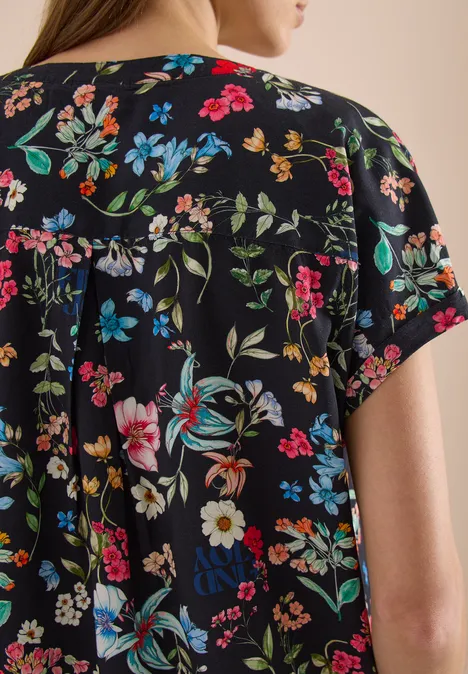 Rückenansicht einer Frau in kurzärmligem schwarzem Shirt mit farbenfrohem Blumenmuster.