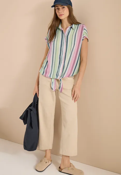 Overhemdblouse met strepen en knopen vanilla white Persoon draagt beige wijde broek en gestreept geknoopt shirt, met tas en platte schoenen.