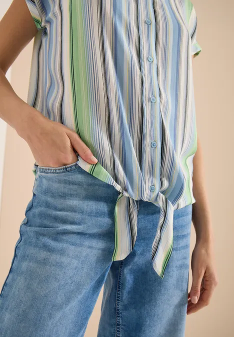 Person trägt blaue Jeans und gestreiftes Hemd, geknotet an der Taille, Hand in Tasche.