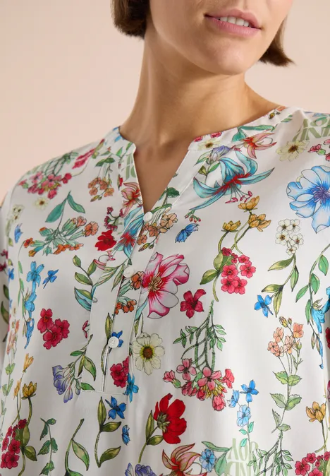 Femme porte un chemisier blanc à motifs floraux colorés et col en V.