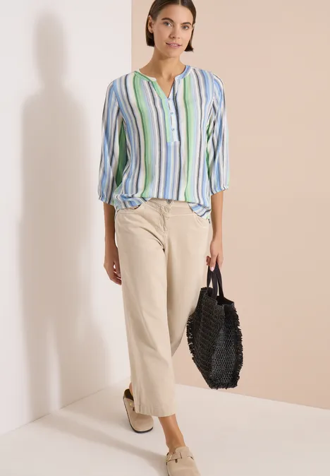 Chemisier à manches 3/4 avec rayures multicolores light sky blue Femme en chemisier rayé, pantalon ample clair, chaussures à semelle compensée blanches et sac tressé noir.