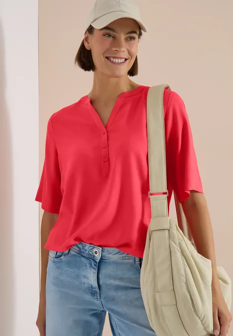 Blouse met korte mouwen en gespleten hals coral Vrouw met rood shirt, blauwe jeans en beige schoudertas.