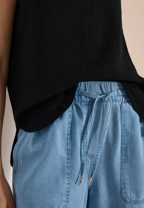Person trägt schwarze Bluse und hellblaue Jeanshose mit Tunnelzug und aufgesetzten Taschen.