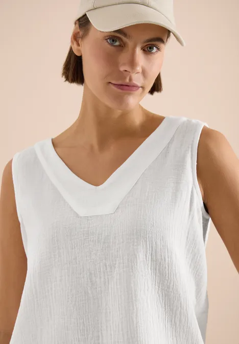 Frau in weißer Kappe und ärmellosem, strukturierten V-Neck-Oberteil.