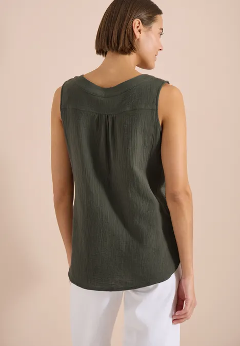 Rugaanzicht van een vrouw in een mouwloos olijfgroen topje voor een lichte achtergrond.