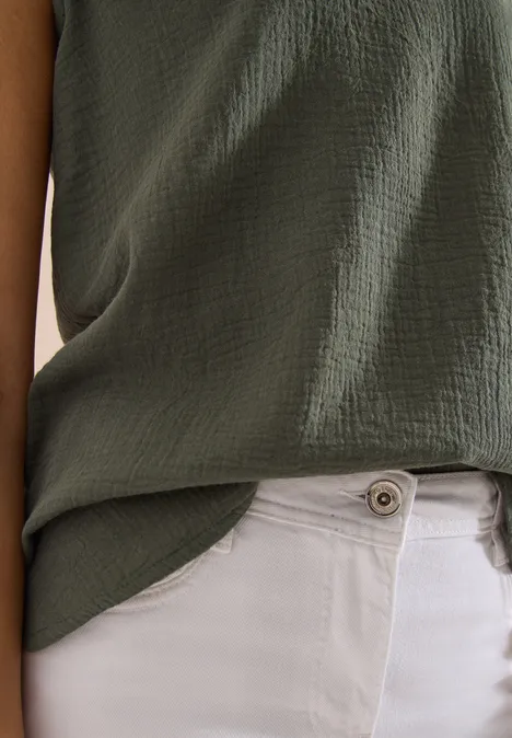 Foto van een persoon met een groen, gestructureerd shirt en witte broek, close-up van bovenlichaam.