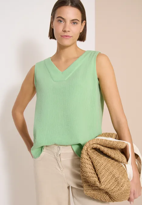 Vrouw in lichtgroene mouwloze V-hals top, beige broek en gevlochten tas