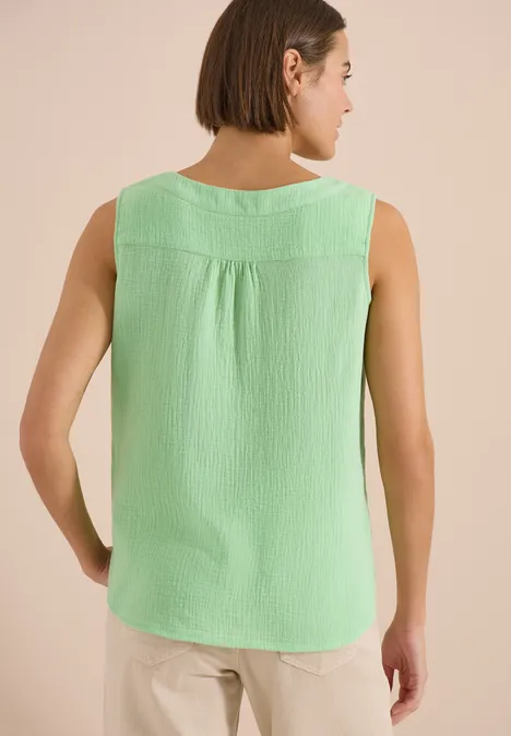 Achteraanzicht van een vrouw in een lichtgroen topje met structuur en een beige broek.