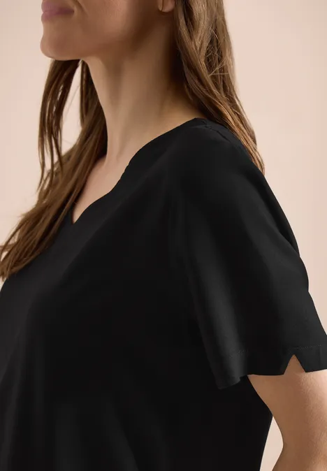 Eine Frau im Profil trägt ein schlichtes schwarzes T-Shirt mit V-Ausschnitt und kurzem Ärmel.