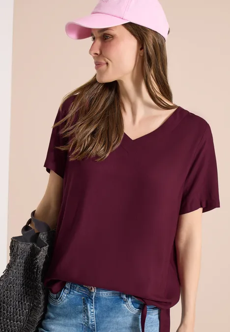 Frau trägt weinrotes V-Ausschnitt-T-Shirt mit kurzen Ärmeln und Jeans.