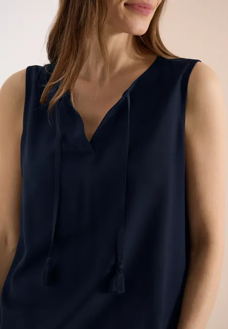 Frau in dunkelblauem, ärmellosem Top mit V-Ausschnitt und Quastenbändern