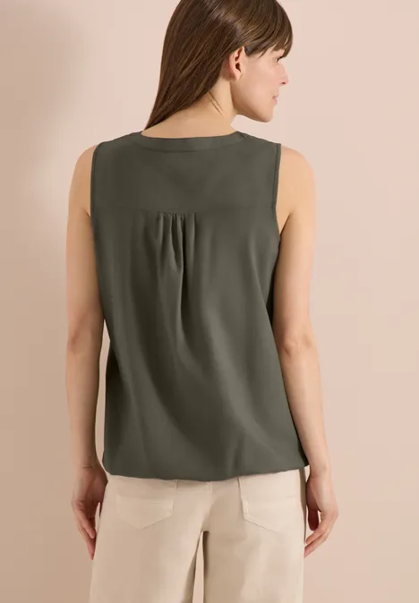 Frau von hinten in olivgrüner ärmelloser Bluse und beigefarbener Hose.