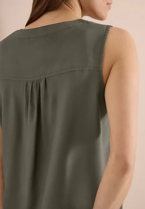 Rückansicht einer Frau in einem ärmellosen, khakigrünen Oberteil mit Falte unter dem Rückenpasse.