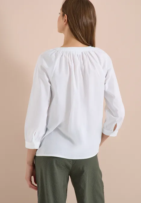 Vrouw van achteren met witte blouse en groene broek voor een neutrale achtergrond
