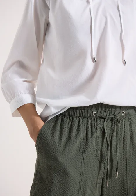 Witte blouse met driekwart mouwen en donkergroene, gestructureerde broek met trekkoord en zakken.