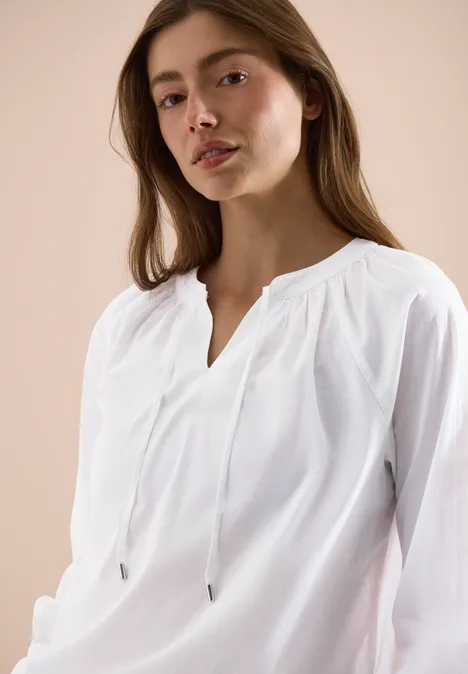 Vrouw met wazig gezicht draagt losse witte blouse met V-hals voor lichte achtergrond.