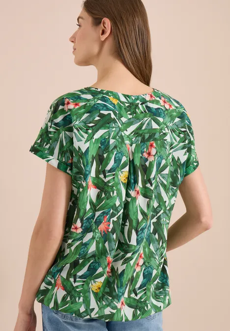 Vrouw van achter in korte mouw blouse met groene bladerenprint.