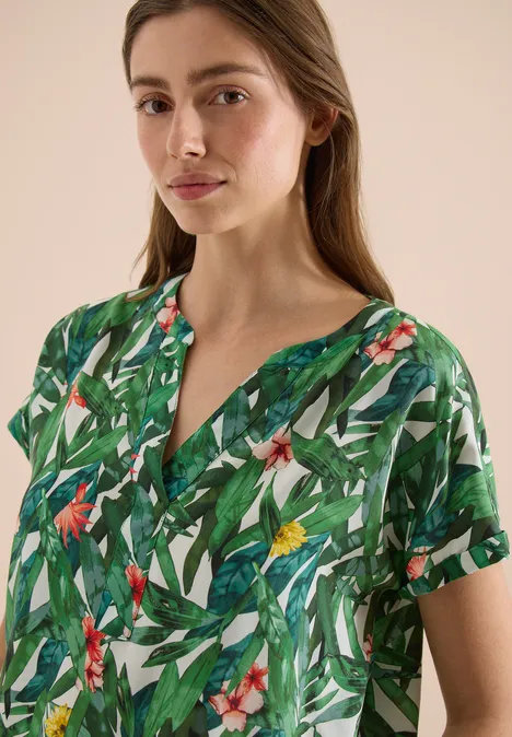 Vrouw draagt kortmouwige blouse met groen tropisch patroon.