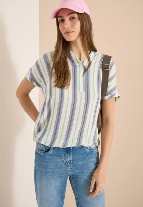 Frau in gestreiftem Hemd und Jeans vor hellem Hintergrund, Gesicht unkenntlich.