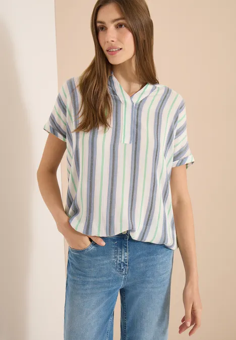 Frau in kurzärmligem, pastellgestreiftem Hemd und blauen Jeans.