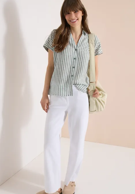 Eine Person trägt grünes, gestreiftes Kurzarmhemd, weiße Hose und trägt eine Handtasche.