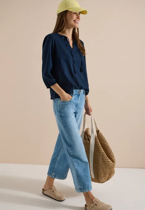Frau in lässigem Outfit: dunkelblaue Bluse, weite Jeans, Cap, Tasche und Sandalen.